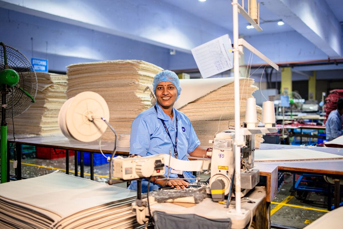 A factory worker smiling beside rolls of fabric